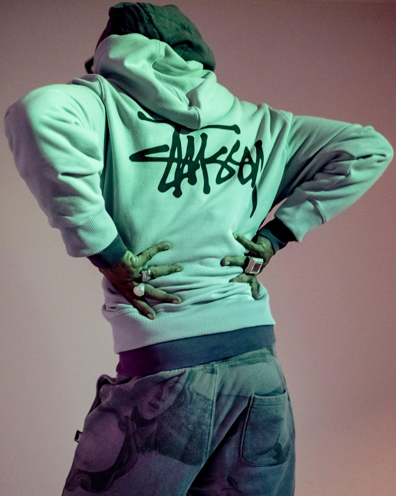 A person wearing a light-colored hoodie with graffiti-style writing on the back.