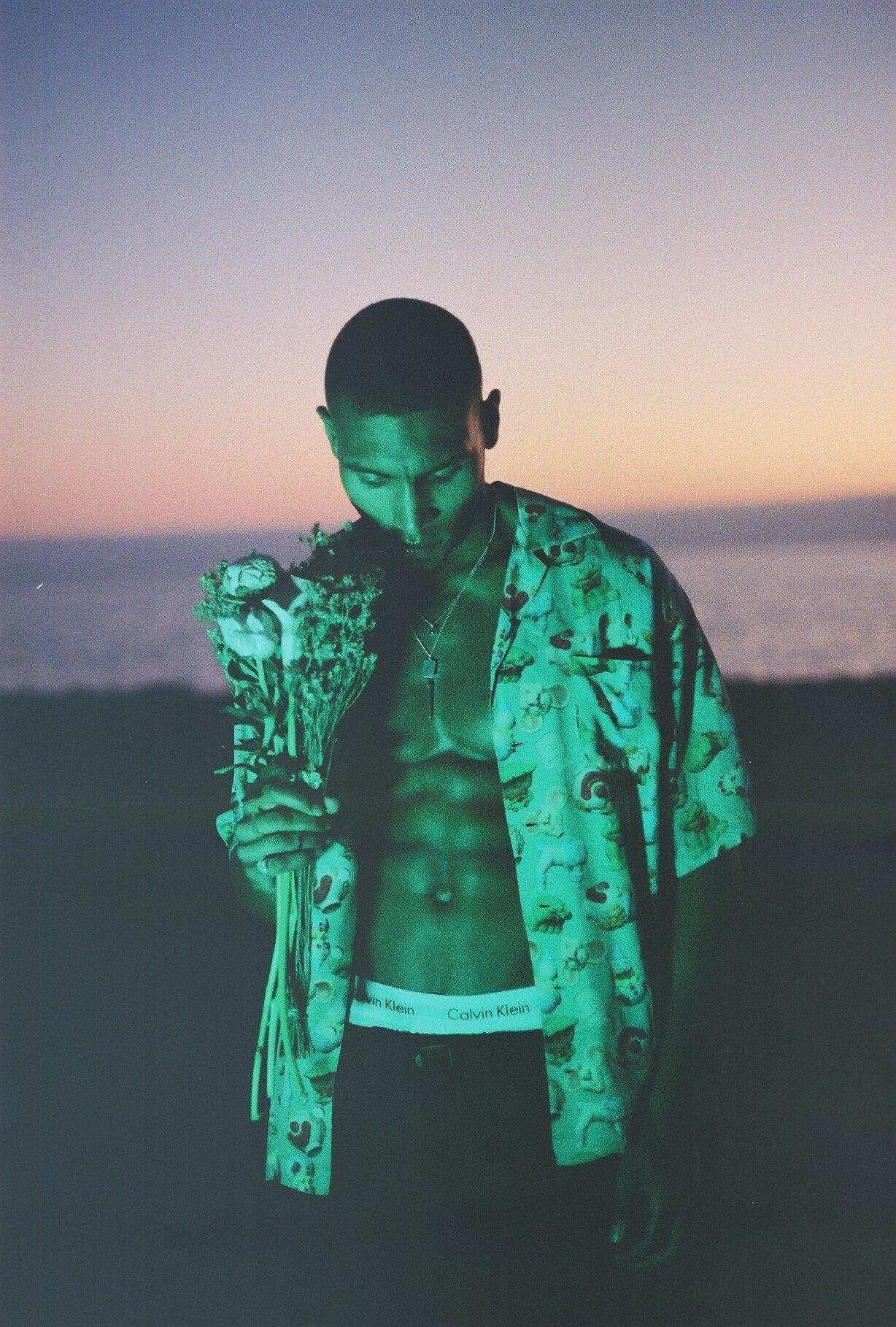 Man posing with an open shirt and a flower bouquet for Visual installment 3.