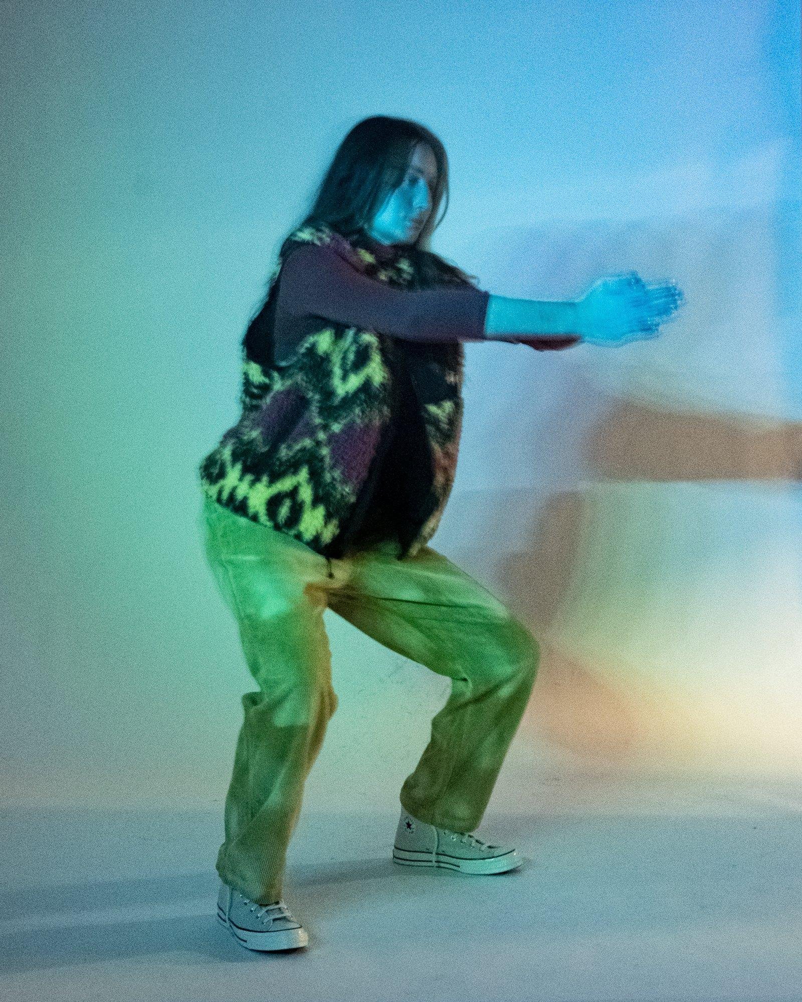 Model posing for Visual Instalment 9 in blue and green lighting.