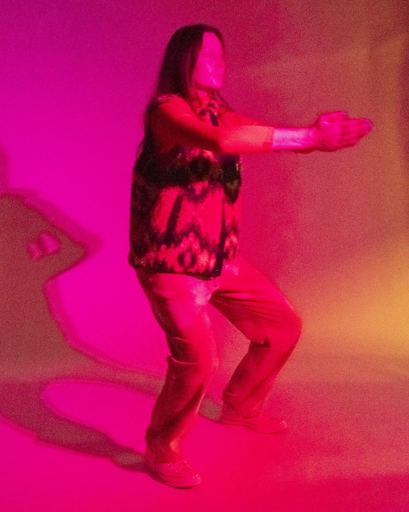 Model posing for Visual Instalment 9 in pink and red lighting.