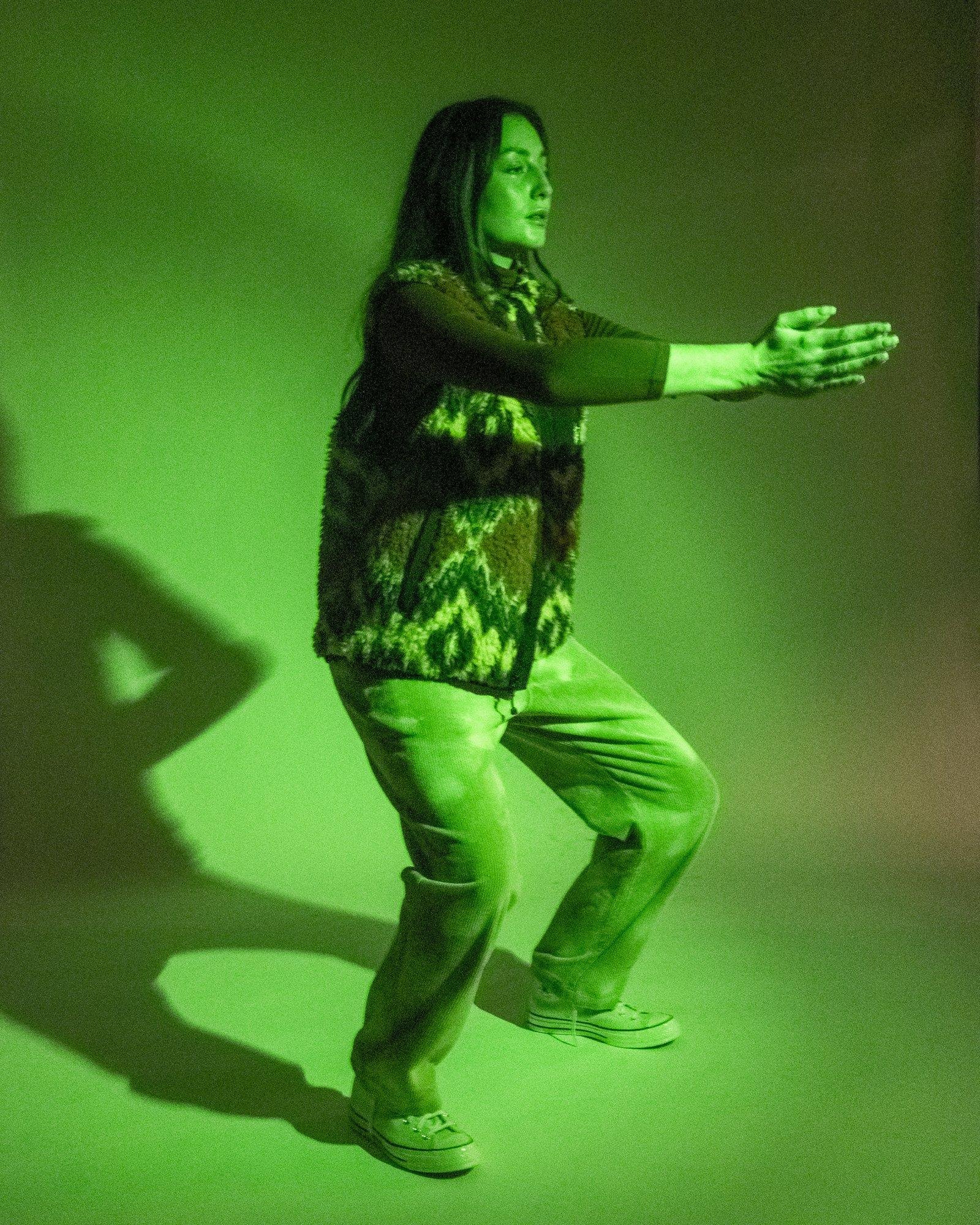 Model posing for Visual Instalment 9 in vibrant green lighting.